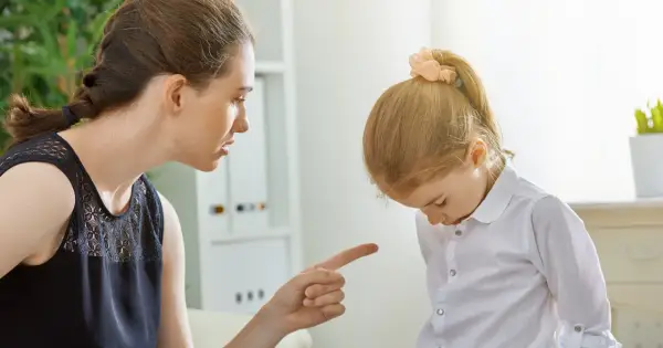 Matka karci córkę za złe zachowanie, wskazując palcem. Dziewczynka spuszcza wzrok, zawstydzona.